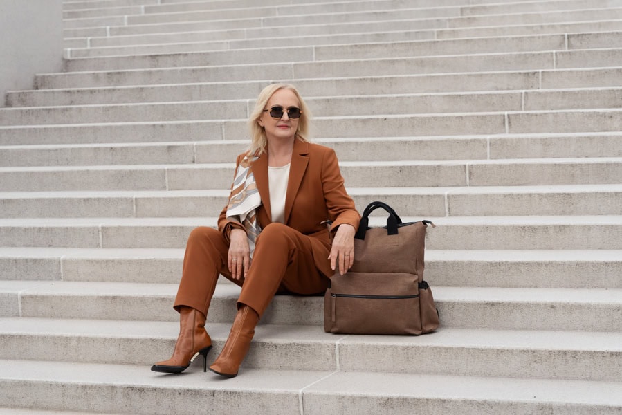 Produktų fotografija – moteris elegantiškoje aprangoje pasirėmusi į rudą krepšį, miesto stiliaus vizualas sukurtas „Subtilūs vizualai“ fotografija.