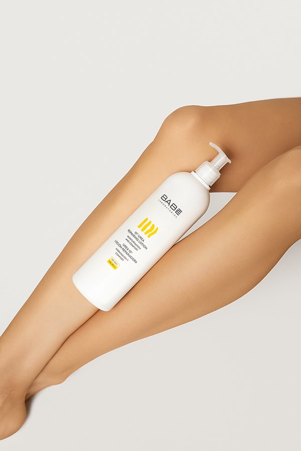 Produktų fotografija studijoje „Subtilūs vizualai“ – „BABÉ“ kūno losjonas kompozicijoje su moters kojomis šviesiame fone.